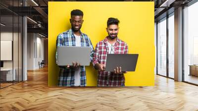 Portrait of a two mixed race men holding laptops isolated over yellow background Wall mural